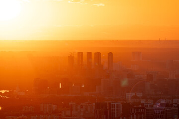 A breathtaking aerial view of the modern city skyline during a golden sunset. The cityscape, with skyscrapers and residential buildings, is bathed in the warm rays of the evening sun. © hodim