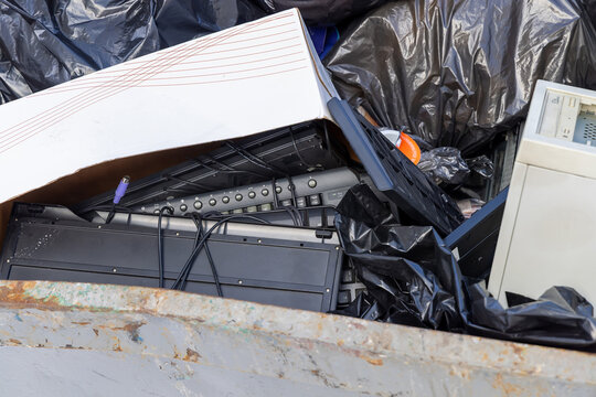 Pile of discarded computer keyboards and electronic components in a recycling bin. Electronic waste management and hardware disposal. Concept of technological obsolescence and pollution