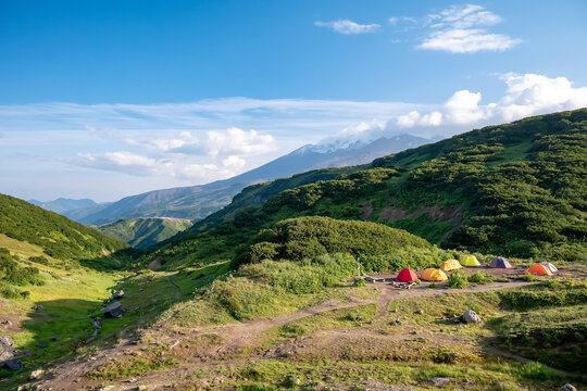 A vibrant campsite in a lush green valley with tents under clear blue skies and mountain views, allowing you to enjoy the beauty of nature and outdoor adventures. Tourism and Healthy Lifestyle