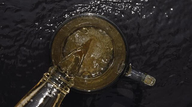 Overhead View of Golden Beer Pouring into Frothy Mug on Wet Black Surface
