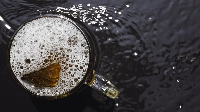 Top View of Frothy Beer Mug on Dark Rippling Water Surface
