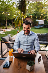 Fototapeta premium Mid adult man remote working on laptop in backyard