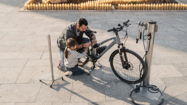 Father and young daughter repairing a bicycle together at a public bike station in the city