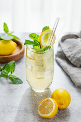 Fototapeta premium A summer drink with lemon, mint, and ice in a glass against a sunny window background.