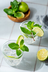 Fototapeta premium A fresh mojito with lime, mint and ice in glasses. Citrus lemonade or cocktail on a tile background