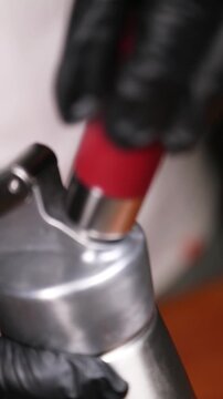 Chef sellando un sif&oacute;n y cargando un cartucho de gas para espuma. Chef profesional con guantes negros cerrando el sif&oacute;n e insertando la carga de gas. T&eacute;cnica de gastronom&iacute;a molecular.