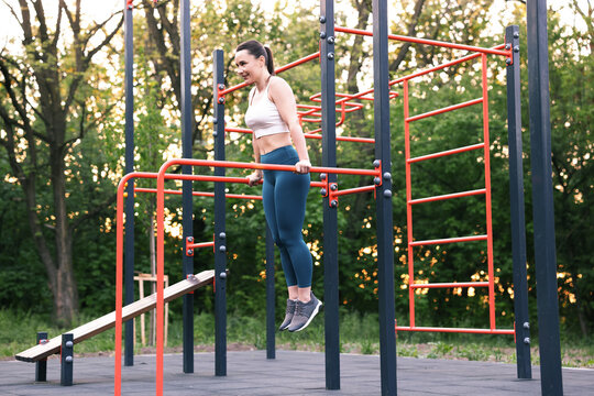 Athletic woman exercising on parallel bars at outdoor gym
