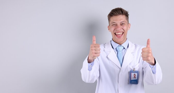 Medical assistant showing thumbs ups gesture on light grey background. Space for text