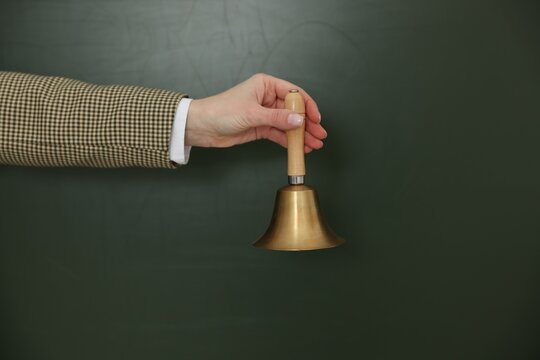 School holidays. Teacher ringing golden bell near chalkboard, closeup. Space for text