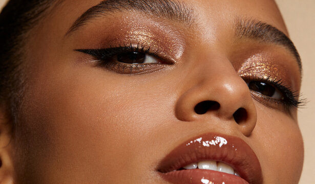 Woman with glowing golden eyeshadow and glossy lips. Extreme close-up shot of professional makeup look. Beauty industry concept for cosmetic branding and skin care advertising.