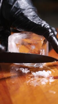 Barman tallando y dando forma a un cubo de hielo para c&oacute;ctel. Barman profesional cortando y perfilando un cubo de hielo a mano. C&oacute;ctel artesanal, t&eacute;cnica de tallado de hielo artesanal.