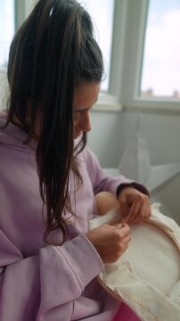 Casual woman focuses on detailed embroidery near window