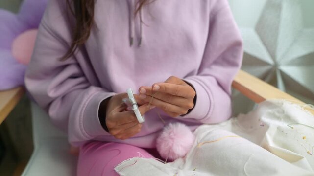 Female crafting colorful pink pompom with scissors while seated
