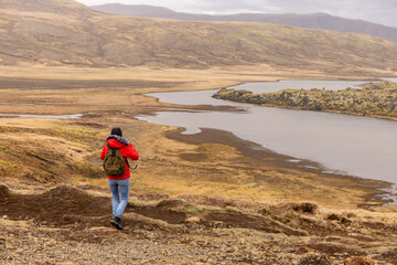 Fototapeta premium Randonneuse qui contemple la vue panoramique d’une vallée islandaise avec rivière et terrain volcanique 