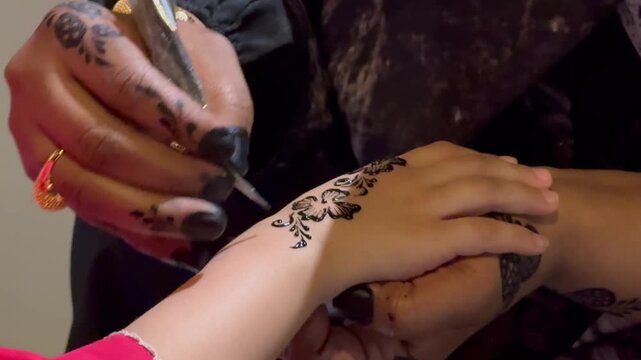 Professional artist applying traditional black henna tattoo design on a little girl hand for eid celebration