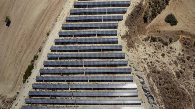 Rows of solar panels installed on a dry hillside in Cyprus, capturing sunlight to produce clean electricity and contributing to sustainable energy development. Aerial top down view, drone flight