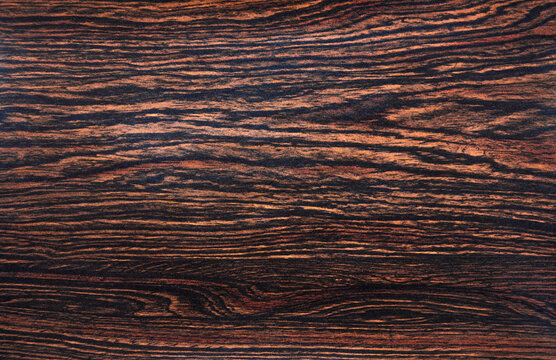 Photo of the background texture made of dark makassar wood.Dark wooden background for the text.The material for finishing luxury furniture.