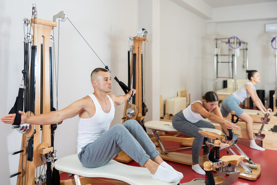 Active young man doing arm exercises on cable training device in well-equipped gym