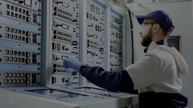 Technician in blue uniform working on electrical control panel with buttons and switches