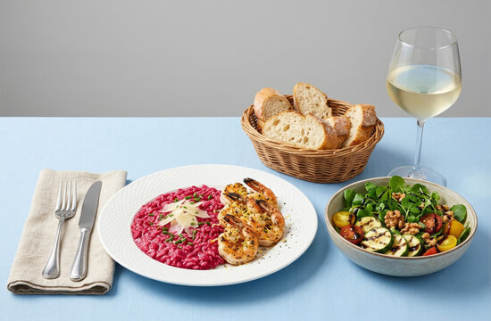 Beetroot risotto dish with grilled shrimp served with salad and white wine.