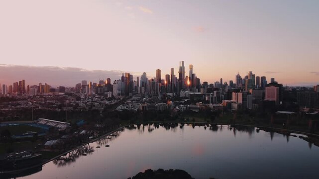 Aerial drone view Melbourne CBD skyline and Albert Park Lake at sunset golden hour Australia 4K