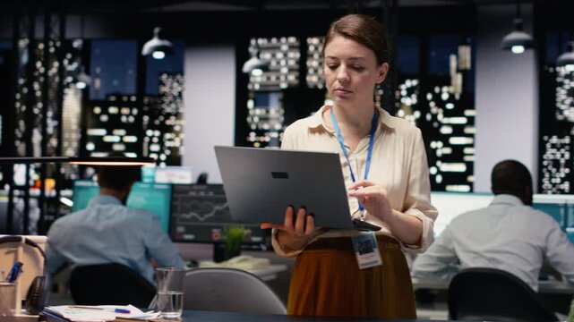 Portrait of smiling businesswoman coordinating daily administrative operations with laptop. Happy woman standing in office uses device to implement sales strategies increasing profitability.