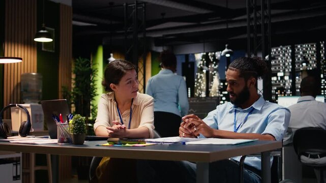 Cheerful coworkers doing fist bump pleased by business results, middle eastern man in wheelchair celebrating task success with his manager. Disability friendly office workspace late at night.