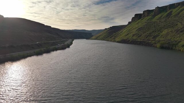 Low drone flyover along the Boise River near Diversion Dam, moving toward Lucky Peak Dam, Idaho. Canyon walls flank the river with cars driving on Highway 21.

