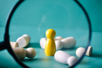 A conceptual stock photo of a single yellow wooden peg doll standing upright while surrounding white figures are fallen and scattered. © Akram