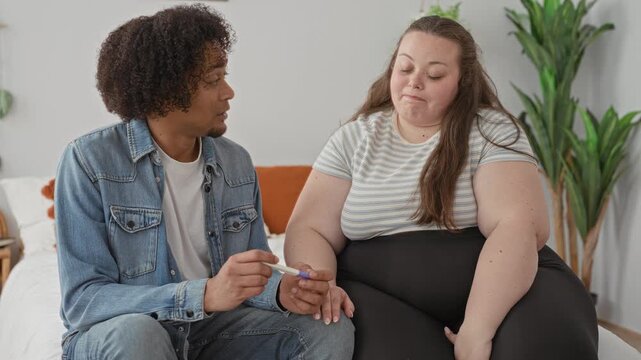 Woman holds pregnancy test on bed while partner takes her hand and they exchange quiet focused looks; uncertainty support.