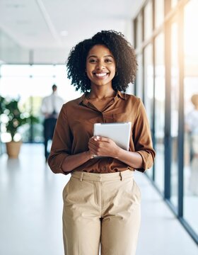 Smiling businesswoman holding tablet in office hallway, brown blouse and beige trousers, corporate office, modern workplace