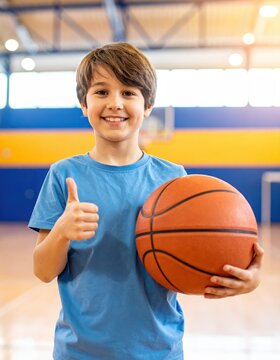 Smiling boy with basketball and thumbs up in indoor gym, youth sports training, active lifestyle