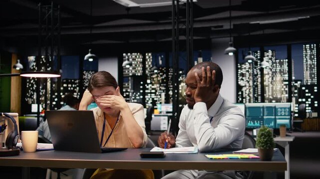 Burnout and frustration, two colleagues struggling to stay awake and solve tasks, worried of missing deadline late at night. Diverse people with low energy and exhaustion overwhelmed by work.