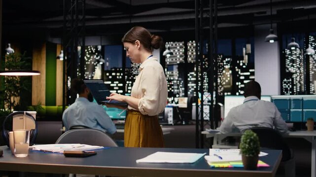 Standing in office at night, woman entrepreneur uses laptop, ensuring profitability and efficiency for strategy and action plan. Manager working on business growth by studying forecast.