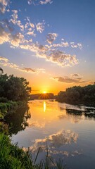 Obraz premium Golden Sunset Reflecting on Calm River Between Lush Green Trees