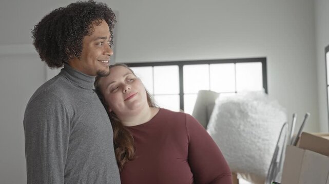 Man and plus size woman lean together with head on shoulder, holding moving boxes inside building; affection moving together.