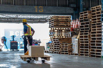A logistics worker pulling a hand pallet jack loaded with a cardboard box towards a shipping dock...