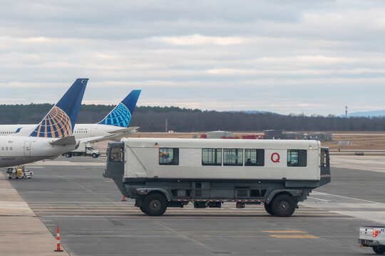 Washington Dulles International Airport, Virginia, USA - January 2, 2024 - Historic Dulles Mobile Lounge passenger transfer vehicle on the ramp at IAD with United Airlines jet tails visible behind