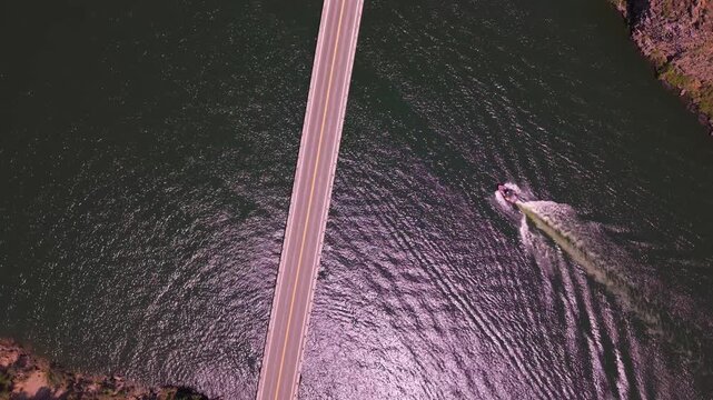 Aerial drone shot of speedboats racing under the Highway 21 bridge on Lucky Peak Reservoir, Idaho. Fast powerboats creating wakes on the sparkling water with scenic canyon backdrop.