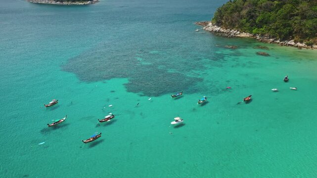Thailand travel destination. Aerial view drone flight over calm, clear turquoise ocean waters, tropical islands with traditional longtail boats anchored in bay, coral reefs and lush green coastline