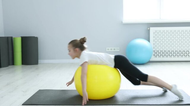 Cute little girl exercising with fitness ball indoors