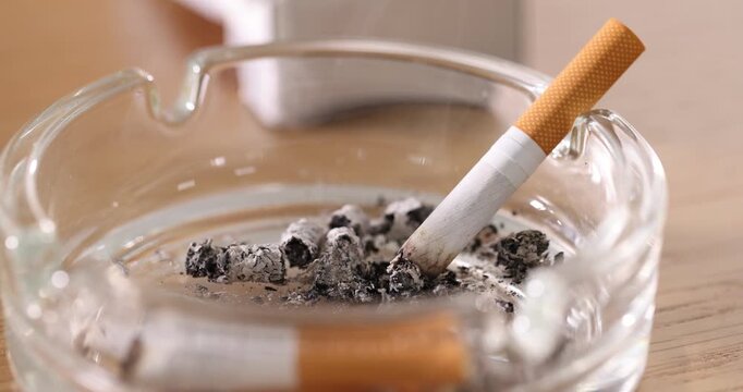 Cigarette butt smoldering in ashtray on wooden table, closeup