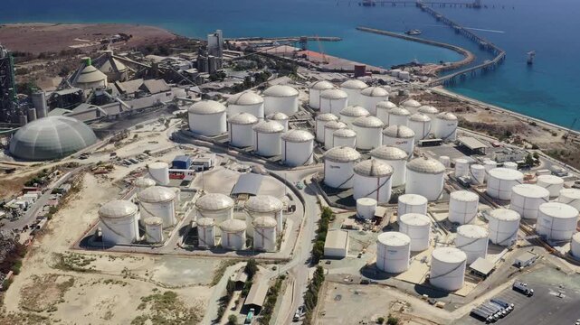 Large oil storage tanks and an industrial complex line Cyprus coast with a long pier extending into the Mediterranean Sea, representing energy infrastructure and global trade. Aerial view drone flight