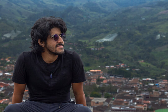 Hombre con barba y cabello largo sentado con camisa negra y lentes oscuros mirando al lado derecho en Jard&iacute;n, Colombia