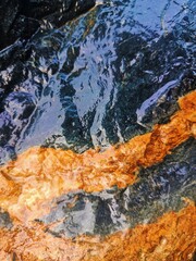 Naklejka premium Vertical shot of a wet geological mining ore face showcasing a prominent golden-orange iron oxide band contrasting against glossy dark blue bedrock.