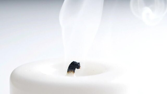 Wisps of white smoke gracefully ascend from a freshly extinguished candle wick, symbolizing a quiet conclusion and moments of serene reflection in a tranquil setting
