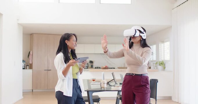 Female team watching tablet prompt guiding VR tester in headset testing VR controls in kitchen