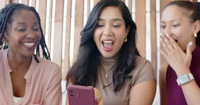 Diverse female friends watching center woman tapping mauve smartphone, sharing content on bench