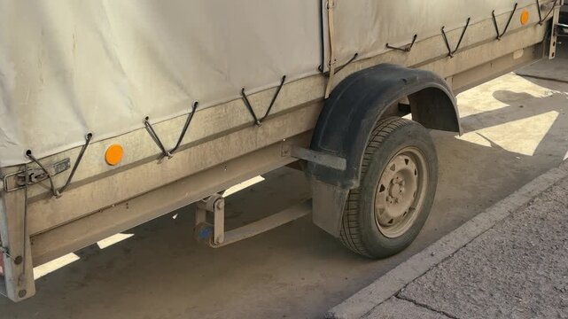 Tarp covered trailer parked on asphalt dirty after long trip, closeup of mud splattered wheel and bent fender, canvas secured