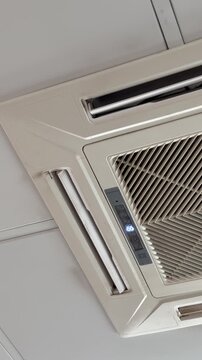 Ceiling cassette air conditioner unit mounted in suspended office ceiling grid, white grille and vents, closeup inspection